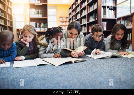 Lehrer, Kinder und Bücher auf dem Boden, Liegen und Lesen in der Bibliothek, Bildung und Lernen für die Zukunft. Frau, Kinder und entspannen Sie sich auf dem Teppich mit Lernen Stockfoto