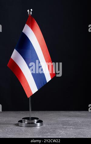 Thailändische Flagge auf Metallständer auf grauem Tisch vor dunklem Hintergrund Stockfoto