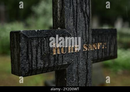 Hintergrundaufnahme des Granit-Gedenkkreuzes mit graviertem goldenem Epitaph zeigt den Ruhe-Schacht, der auf einem düsteren Friedhof steht. Regennass Grabmarker mit Spuren der Zeit zum Gedenken an das Verstorbene, Kopierraum Stockfoto