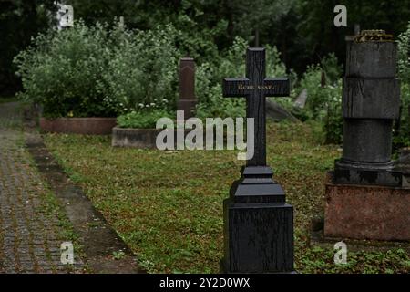 Hintergrundaufnahme des regennassen Gedenkkreuzes, das als dauerhafte Gedenkstätte für den Verstorbenen auf einem düsteren Friedhof dient. Schwarzer Grabstein mit graviertem Epitaph steht Ruhe-Schaft, Kopierraum Stockfoto