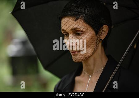 Porträt einer trauernden Seniorin im Trauerschleier, die auf den Grabstein herabblickt, während sie sich vor Regen unter schwarzem Schirm versteckt, Kopierraum Stockfoto