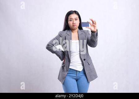 Ausdruck der schönen jungen Bürofrau, die hockt, Taille hält und Debit-Kreditkartenmitglied trägt grauen Anzug, der isoliert auf weißem Hintergrund steht. Stockfoto