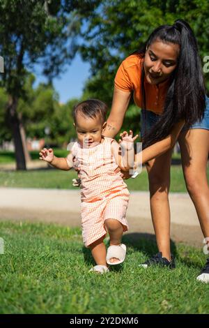 Die einjährige Latina Baby macht mit Hilfe ihrer Mutter ihre ersten Schritte in einem Park im Freien Stockfoto