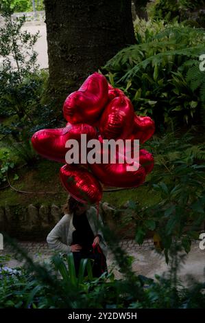 In Quinta da Regaleira schweben leuchtend rote Ballons in Herzform vor einer üppigen Gartenkulisse Stockfoto