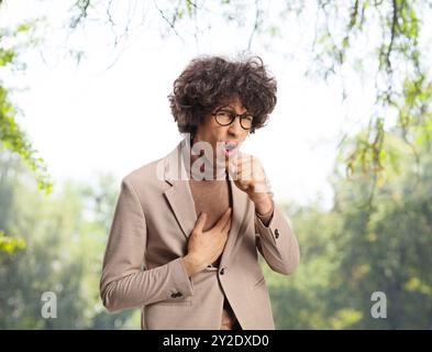 Junger Mann mit Heuschnupfen, der in einem Park hustet Stockfoto