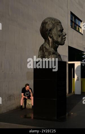 Ein Mann raucht eine Zigarette hinter der Büste von Nelson Mandela vor der Royal Festival Hall, Southbank, London, Großbritannien. Juni 2024 Stockfoto