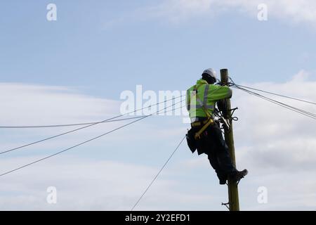 OpenREACH Telefontechniker an der Spitze eines Telegrafenmasts oder Versorgungsmasts zur Verkabelung von Telefonleitungen Stockfoto