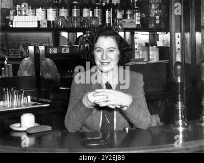 Eine Dame hinter der Hotelbar mit Flaschen und Preisen und einem Bierpumpengriff. Aus einer Broschüre für das Red Lion Hotel, High Wycombe, Buckinghamshire, England. Undatiert, aber Mitte Ende der 1930er Jahre: Dies basiert auf historischen Notizen, Stilen und dreistelligen Telefonnummern. Zu dieser Zeit gehörte das Hotel „Mogford’s“. Stockfoto