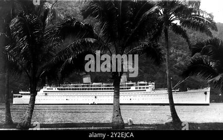 Aus einem alten Foto: Undatiert, um 1950, ein langes Schiff mit zwei Trichtern, Palmen im Vordergrund. Es handelt sich um die SS Monterey in Pago, Pago, Amerikanisch-Samoa. Stockfoto