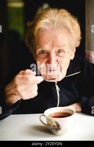 Eine ältere Frau sitzt bequem in ihrem gemütlichen Zuhause und genießt eine warme Tasse Tee. Stockfoto