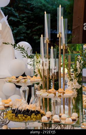 Eleganter Hochzeits-Desserttisch mit Kerzenlicht und Blumendekor im Freien. Stockfoto