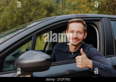 Ein glücklicher Fahrer zeigt Daumen hoch und lächelt in die Kamera im Auto. Stockfoto
