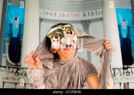 Digital verbessertes Bild eines maskierten Schauspielers in einem physischen Theater mit einem antiken griechischen Bühnenhintergrund Stockfoto