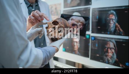 Männliche und weibliche Wissenschaftler studieren Anatomie des fossilen Schädels des alten Mannes mit einem Tablet-Computer. Archäologen arbeiten im archäologischen Labor. Platine mit gedruckten Bildern der 3D-Visualisierung des menschlichen Kopfes. Stockfoto