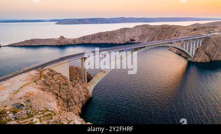 PAG-Brücke mit fahrenden Fahrzeugen über den Kanal des Adriatischen Meeres bei Sonnenuntergang. Das Straßennetz verbindet die Insel mit dem kroatischen Festland und bietet eine atemberaubende Aussicht Stockfoto