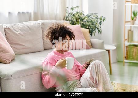 Eine junge Frau genießt ein warmes Getränk und blättert in einer ruhigen Umgebung durch ihr Telefon. Stockfoto