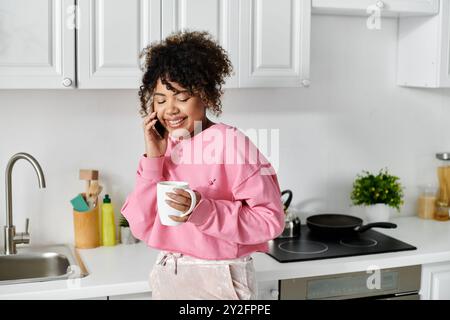 Lächelnde Frau chelt am Telefon, während sie zu Hause eine warme Tasse hält. Stockfoto