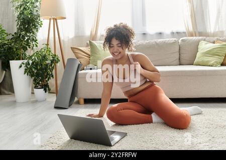 Eine fröhliche Frau greift auf ihren Laptop, während sie auf dem Boden sitzt. Stockfoto