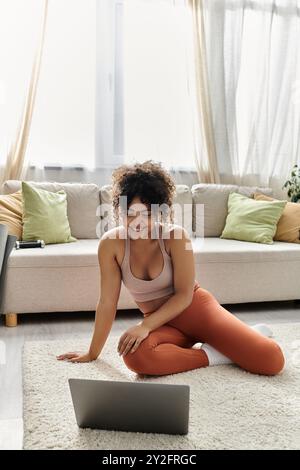 Eine junge Frau greift in einem gemütlichen Wohnzimmer glücklich mit ihrem Laptop in Berührung. Stockfoto