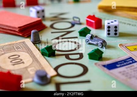 Ein Monopolbrett mit Spielstücken, darunter Geld, Häuser, Hotels, Schuhwürfel, Chance- und Community-Brustkarten. Stockfoto