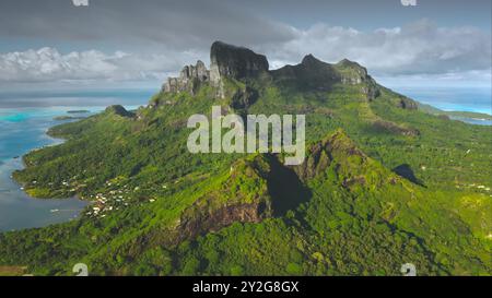 Die Drohne fängt die atemberaubende Landschaft der grünen tropischen Insel Bora Bora ein, den Berg Otemanu, der sich über der Lagune mit kristallklarem Wasser erhebt, und das kleine Küstendorf. Exotische wilde Natur, Reise aus der Luft Stockfoto