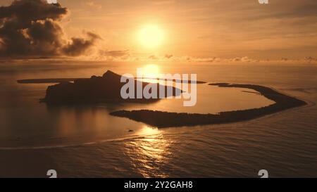 Blick aus der Vogelperspektive heller orangefarbener Sonnenuntergang über der tropischen Insel Maupiti in Französisch-Polynesien, mit Blick auf die Lagune, die hellen Sonnenwolken, den Himmel, das Riff und die Wellen, die das Barriereriffmeer durchbrechen. Wunderschöne Naturlandschaft. Stockfoto