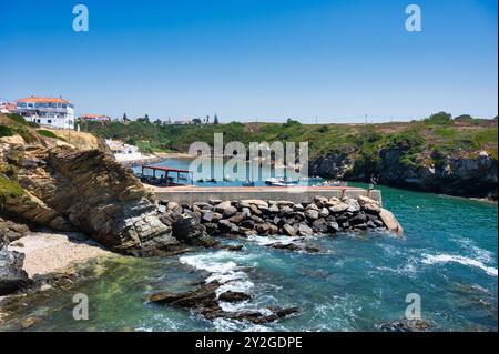 Felsige Küste mit einem kleinen Hafen und Booten auf dem blauen Wasser von Porto Covo, einem Fischerdorf in Alentejo, Portugal. Stockfoto