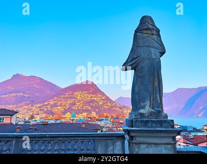 Die Skulptur auf der Terrasse der Kathedrale von San Lorenzo gegen den Monte Bre und Monte Boglia im hellen Sonnenuntergang, Lugano, Schweiz Stockfoto