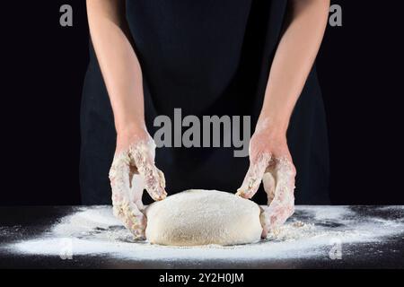 Weibliche Hände bereiten Pizzateig auf einem dunklen Tisch zu. Lebensmittelkonzept Stockfoto