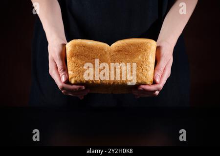 Baker Woman hält warmes hausgemachtes Brot auf schwarzem Hintergrund Stockfoto