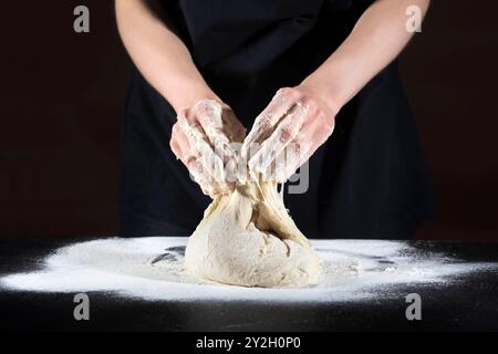 Weibliche Hände kneten den Teig auf einem schwarzen Holztisch. Lebensmittelkonzept Stockfoto