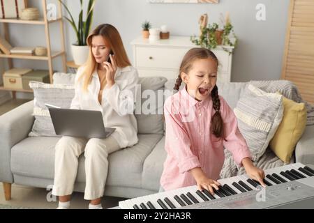 Lautes kleines Mädchen, das Synthesizer spielt, während ihre Mutter zu Hause arbeitet Stockfoto