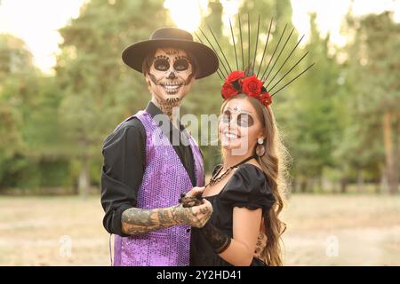 Junge glückliche Paare, die sich für den mexikanischen Tag der Toten (El Dia de Muertos) im Park im Freien angezogen haben Stockfoto