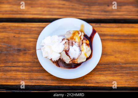 Verschiedene Eissorten mit Schokoladensirup und verschiedenen Belägen auf dem Teller auf dem hölzernen Restauranttisch. Stockfoto