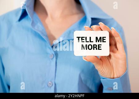 Auf einem weißen Tisch vor einer hellen Ziegelwand, einem Eukalyptuszweig in einer dunklen Vase, einem weißen Becher und einem hellen Holzrahmen mit dem Text, ERZÄHLE MIR MEHR. H Stockfoto