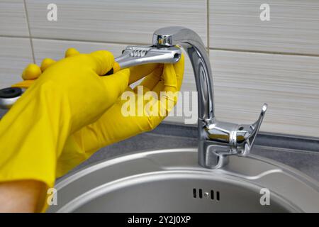 Person in gelben Gummihandschuhen, die den Belüfter für den Wasserhahn mit einem verstellbaren Schraubenschlüssel ersetzt Stockfoto