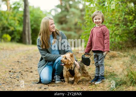 Mutter und ihr kleiner Sohn gehen im Spätherbst-Park mit ihrem Stammhund australischen Terrierhund. Herbstporträt von schwarzem und braunem reinrassigem Au Stockfoto