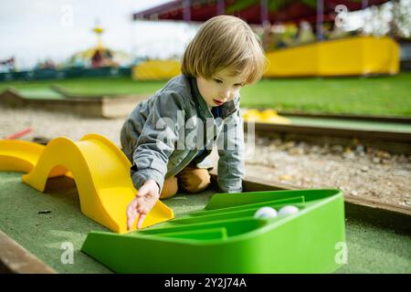 Niedlicher Kleinkinder, der Minigolf spielt und Spaß auf einem Spielplatz im Freien an warmen Herbsttagen hat. Aktive Freizeit für Kinder im Herbst. Stockfoto