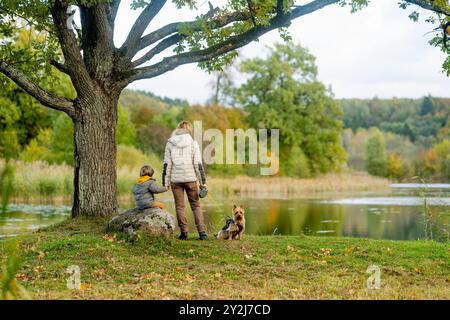 Mutter und ihr kleiner Sohn gehen im Spätherbst-Park mit ihrem Stammhund australischen Terrierhund. Herbstporträt von schwarzem und braunem reinrassigem Au Stockfoto