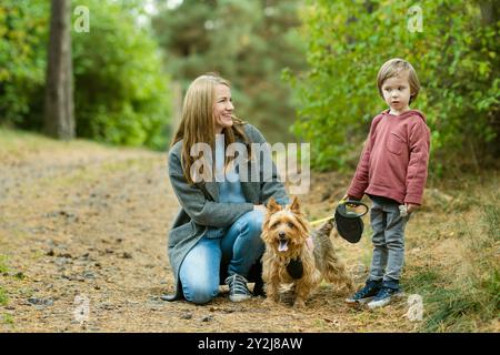 Mutter und ihr kleiner Sohn gehen im Spätherbst-Park mit ihrem Stammhund australischen Terrierhund. Herbstporträt von schwarzem und braunem reinrassigem Au Stockfoto