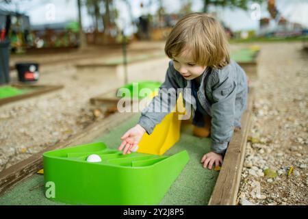 Niedlicher Kleinkinder, der Minigolf spielt und Spaß auf einem Spielplatz im Freien an warmen Herbsttagen hat. Aktive Freizeit für Kinder im Herbst. Stockfoto