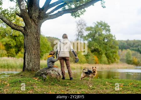 Mutter und ihr kleiner Sohn gehen im Spätherbst-Park mit ihrem Stammhund australischen Terrierhund. Herbstporträt von schwarzem und braunem reinrassigem Au Stockfoto