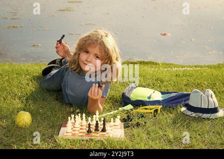 Der Junge zeigt Schachfiguren auf einem Schachbrett. Frühentwicklung. Junge, der über Schach im Sommerpark nachdenkt. Das Konzept des Lernens und der heranwachsenden Kinder. Ausg Stockfoto