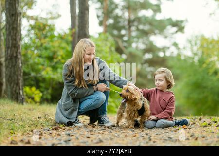 Mutter und ihr kleiner Sohn gehen im Spätherbst-Park mit ihrem Stammhund australischen Terrierhund. Herbstporträt von schwarzem und braunem reinrassigem Au Stockfoto