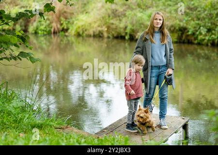 Mutter und ihr kleiner Sohn gehen im Spätherbst-Park mit ihrem Stammhund australischen Terrierhund. Herbstporträt von schwarzem und braunem reinrassigem Au Stockfoto