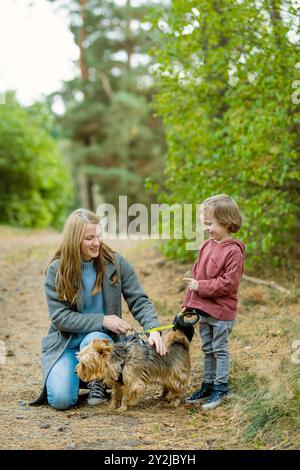 Mutter und ihr kleiner Sohn gehen im Spätherbst-Park mit ihrem Stammhund australischen Terrierhund. Herbstporträt von schwarzem und braunem reinrassigem Au Stockfoto