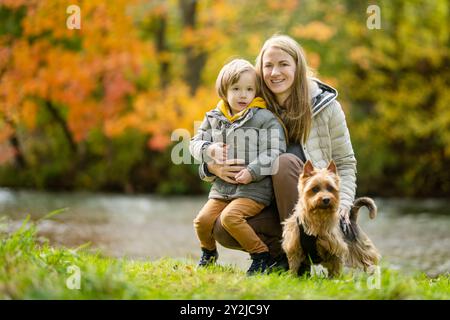 Mutter und ihr kleiner Sohn gehen im Spätherbst-Park mit ihrem Stammhund australischen Terrierhund. Herbstporträt von schwarzem und braunem reinrassigem Au Stockfoto