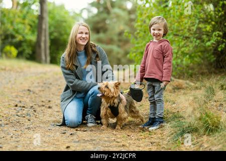 Mutter und ihr kleiner Sohn gehen im Spätherbst-Park mit ihrem Stammhund australischen Terrierhund. Herbstporträt von schwarzem und braunem reinrassigem Au Stockfoto