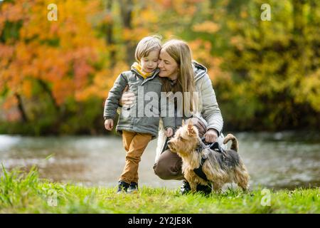 Mutter und ihr kleiner Sohn gehen im Spätherbst-Park mit ihrem Stammhund australischen Terrierhund. Herbstporträt von schwarzem und braunem reinrassigem Au Stockfoto