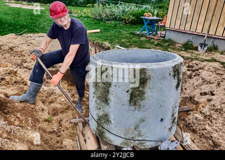 Beim Bau einer Klärgrube in ländlichen Gebieten bewegt der Arbeiter den Betonring mit einem Brecheisen als Hebel. Stockfoto